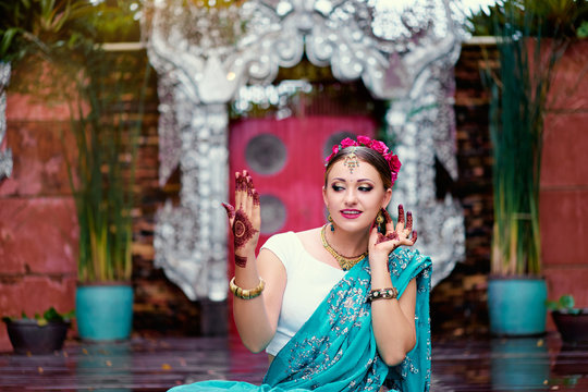 Beautiful young caucasian woman in traditional indian clothing sari with bridal makeup and jewelry and henna tattoo on hands dancing in temple garden.