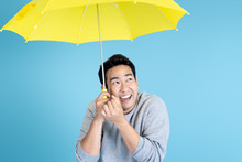 Happy Asian Man Holding Yellow Umbrella On Blue Background.