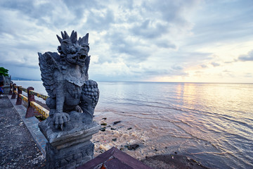 Canvas Print - Art and travel. Hindu stone statue of demon on the sea shore with beautiful sunset view.