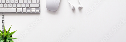 Top view of a white office desk. Copy space. White technology. Keyboard, mouse, headphones and succulent. White on white. Copy space. Panorama