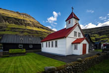 Traditional White Church In Small Village Surrounded With Dramatic Landscape In Faroe Islands.