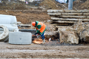 A builder worker in a helmet and a robe works with an industrial iron saw grinder at a construction site with an industrial saw