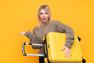 Young blonde woman over isolated yellow background in vacation with travel suitcase