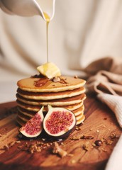 Vertical shot of pancakes with syrup, butter and roasted nuts on a wooden plate