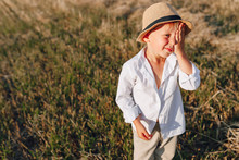 Blond Little Boy In Straw Hat Playing In Field On Mowed Hay. Summer, Sunny Weather, Farming. Happy Childhood.