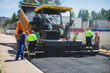 © tsuguliev - Asphalt paver machine and steam road roller during road construction and repairing works, process of asphalting and paving, workers working on the new road construction site, placing a layer