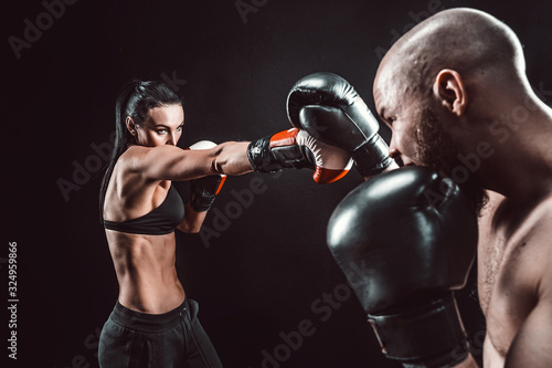 Cuadros en Lienzo Shirtless Woman exercising with trainer at boxing and self defense lesson, studio, dark background