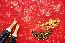 Two Champagne Bottles, Carnival Mask And Confetti On Red Background. Flat Lay Of Purim Carnival Celebration Concept.
