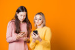 © Alexander - Blonde and brunette with their smartphones on a bright yellow background.