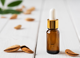 Natural almond essential oil for beauty and spa in a glass bottle. Almonds and green leaves on a white wooden table. Close-up, soft focus.