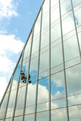 Wall Mural - One window washer works at a height on a high-rise building with a glazed facade against a blue sky with light clouds.