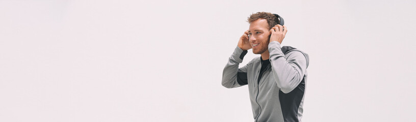 Man listening to music wearing headphones putting them on while walking on white wall header background for fitness gym or home healthy lifestyle sport athlete using wearable technology outdoor.