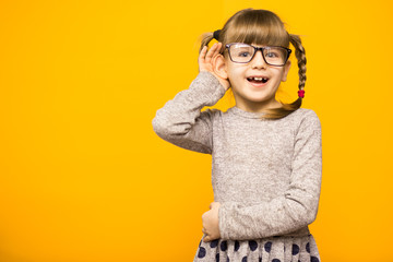 A young child girl journalist in glasses with funny pigtails listening to something holding his hand to ear