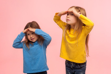portrait of funny amusing two little girls holding hands over eyes and looking far away with curious