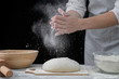 Chef sprinkl flour on a dough for cooking pastries, bread or pizza. Isolated on dark background