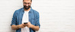 © luismolinero - Handsome man with beard over white brick wall sending a message with the mobile