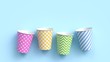 © 3d_kot - Four paper cups with different colorful patterns on blue pastel background