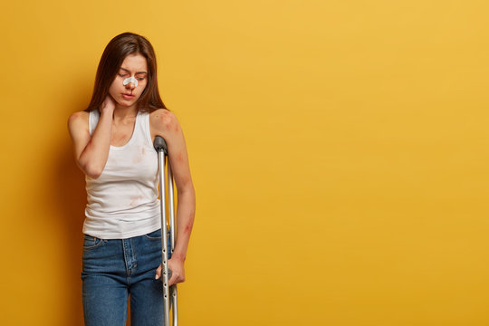 Indoor shot of frustrated woman has accident on motorcycle, touches neck, suffers from pain, recovers for long period at home, focused down and recalls awful details of recent catastrophe on road