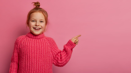 happy foxy girl with hair bun, smiles positively, shows right direction, points away on blank space,