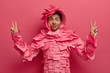 © wayhome.studio  - Surprised funny man has fun in office, poses in creative costume made of sticky notes, raises fingers in victory gesture, shows peace sign, isolated over pink background. Paper outfit. Monochrome