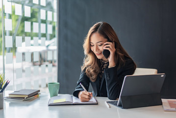happy young asian woman talking on the mobile phone and smiling while sitting at her working place i