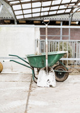 A Green Wheel Barrow In Front Of A Fence With A Dirty Shovel In Front