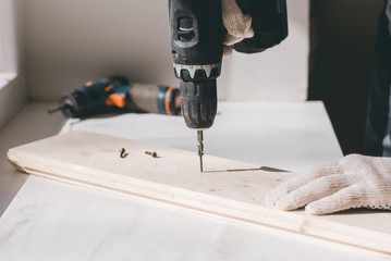 A man holds a cordless screwdriver in his hand and wraps the screw in a Board.