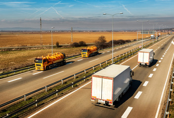 Two Orange Tank trucks or Cisterns passing white Trucks on a countryside Highway traffic through the rural landscape 