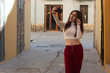 © Sergio Barceló - Portrait of attractive caucasian young woman with magnifying glass taking selfie, in the city, white top and red pants, dark air. Place for your text in copy space.