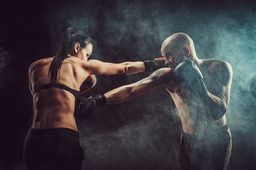 Shirtless Woman exercising with trainer at boxing and self defense lesson, studio, dark background. Female and male fight.