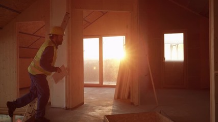 Wall Mural - SLOW MOTION, LENS FLARE: Young builder coming to work early climbs up a ladder into a beautiful sunlit floor under construction. Cinematic shot of a contractor ascending up an extendable ladder.