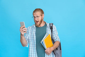 Bearded excited young man student hipster blogger glasses wow emotion hold modern smart phone read good news reply amazed media content surprised shock text message isolated blue studio background.