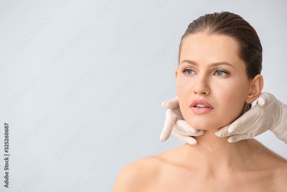 Plastic surgeon touching face of young woman against light background