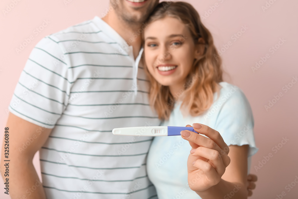 Happy young couple with pregnancy test on color background