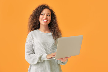 Young African-American woman with laptop on color background