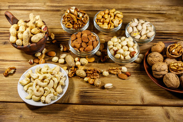 Sticker - Assortment of nuts on wooden table. Almond, hazelnut, pistachio, peanut, walnut and cashew in small bowls. Healthy eating concept