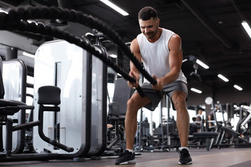 Athletic young man with battle rope doing exercise in functional training fitness gym.