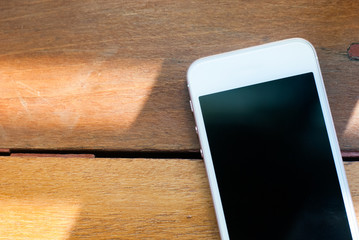 A smart phone with turned-off display placed on a brown wooden table