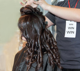 Beautiful girl with curly hair looking away,while female hair stylist positioning head to form a hairstyle