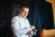 A man fastens cufflinks against the background of his suit. The groom is preparing for the ceremony