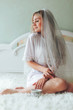 Portrait of a beautiful blonde girl in a Bathrobe with a Cup of tea. The bride in a robe with a veil is sitting on the bed with a Cup of coffee. Morning of the bride