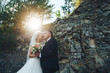 The bride and groom stand against the background of rocks at sunset. Newlyweds at sunset in a mountain forest