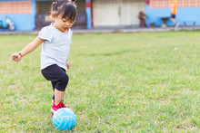 Happy Asian Baby Child Girl Playing And​ Kicking A​ Ball Toys At The Field Playground. She Smiling And Wearing A Blue Shirt. Baby Aged Of 1-2 Years Old. Exercise For Health. Sport And Kids Concept.