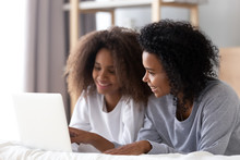 African Mom And Teen Daughter Using Laptop Lying On Bed
