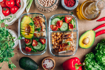 Healthy meal prep containers with chickpeas, chicken, tomatoes, cucumbers and avocados. Healthy lunch in glass containers on beige rustic background. Zero waste concept. Selective focus.