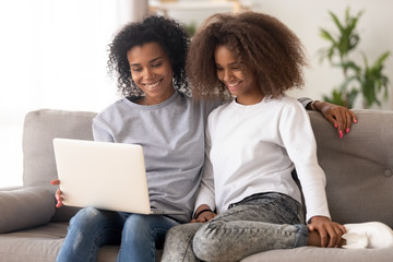 Wall Mural - Happy african family mother and daughter use laptop on couch