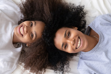 Happy african mother and daughter lying on bed, top view