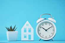 White Retro Alarm Clock And Miniature House On The Blue Backgroumd