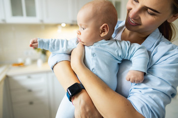 Smiling young lady playing with her baby in the kitchen