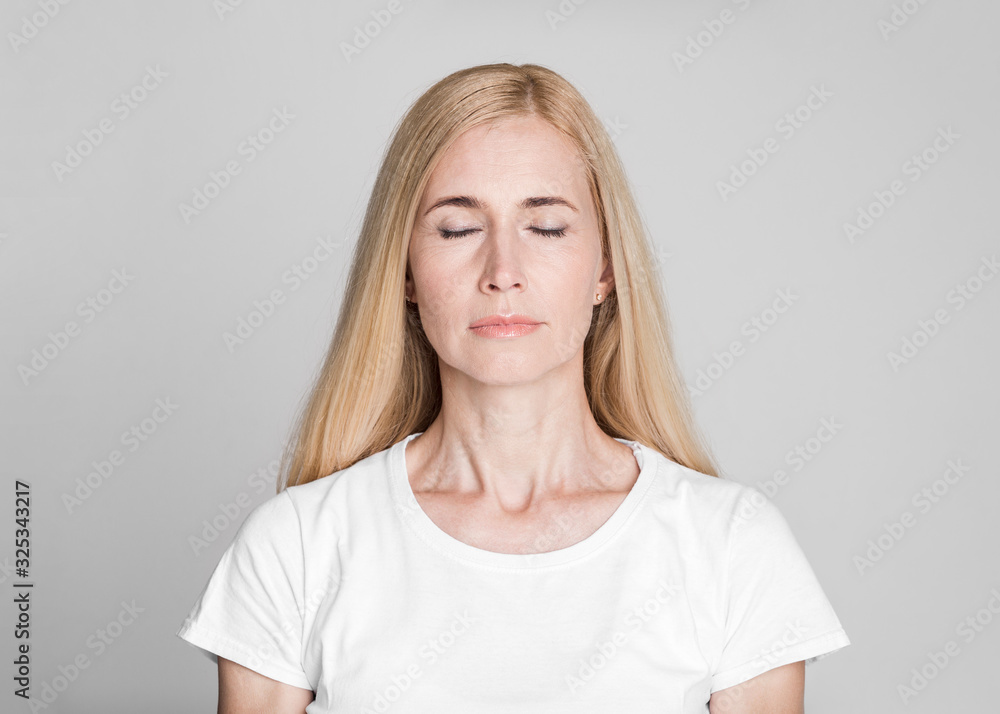 Beautiful middle-aged woman posing with closed eyes - obrazy, fototapety, plakaty 